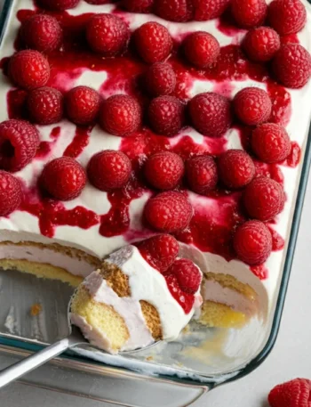 keto White chocolate berrymisu Overhead shot of Keto White Chocolate Berrymisu in a white dish, topped with raspberries and a drizzle of sauce, with a spoonful scooped out.