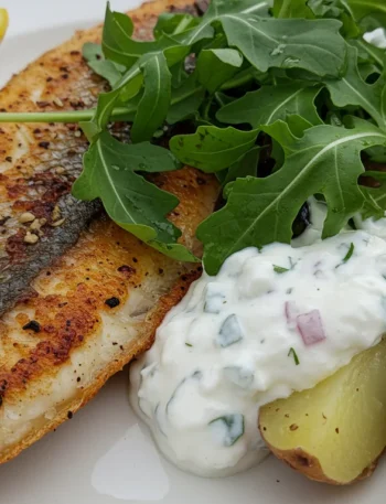 keto Grilled snapper with yoghurt potatoes Close-up of keto grilled snapper with crispy skin, cauliflower salad, rocket, and lemon wedges, captured at a casual handheld angle.